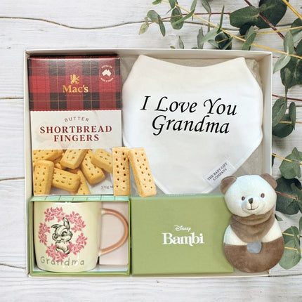 Gift set with cookies, mug, and plush toy in a box labeled 'I Love You Grandma' with eucalyptus leaves in the background.