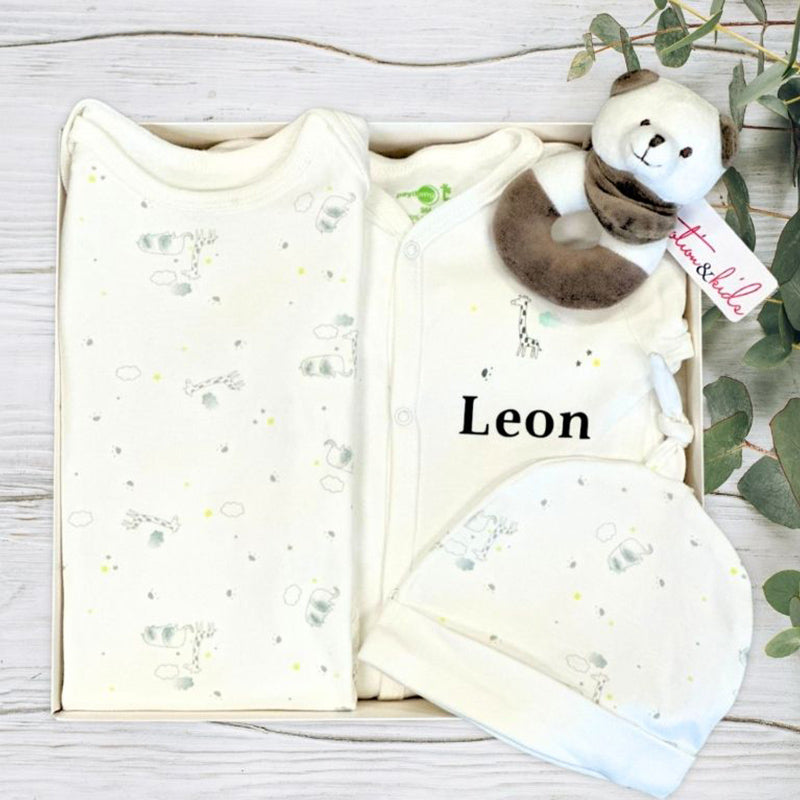 Baby gift box with clothing, baby grow, and teddy bear named 'Leon' on a wooden surface.