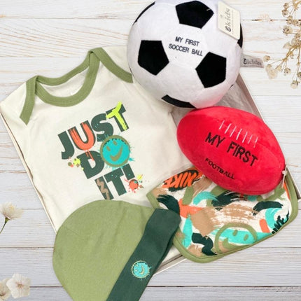 Nike Baby clothing and toys including a romper, hat, bib, soccer ball, and football on a wooden surface.