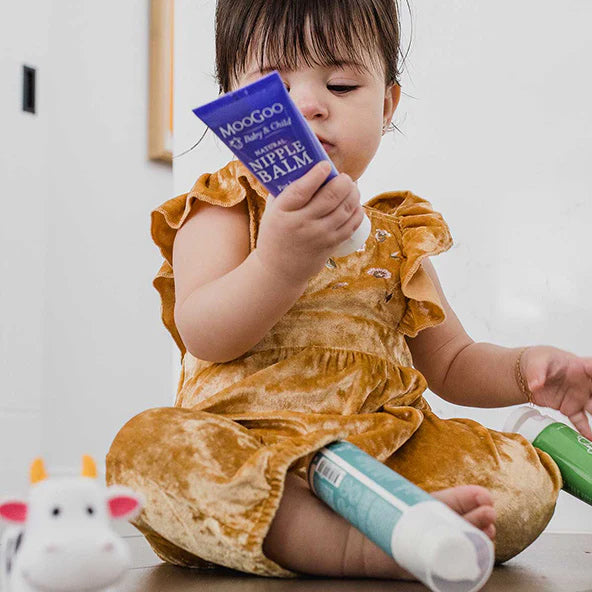 Child holding a purple bottle labeled 'Nipple Balm' with a white background
