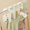 Baby clothes on hangers with size labels against a beige background
