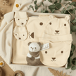 cream baby clothes with face face print, with bear toy. All inside a gift box on pretty surface