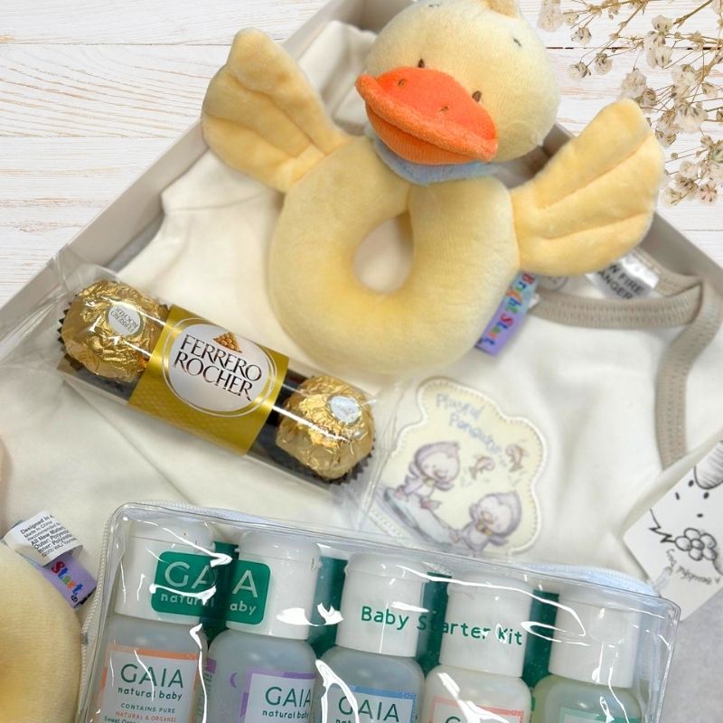 Baby gift set with Ferrero Rocher, plush duck, and GAIA baby products on a white surface.