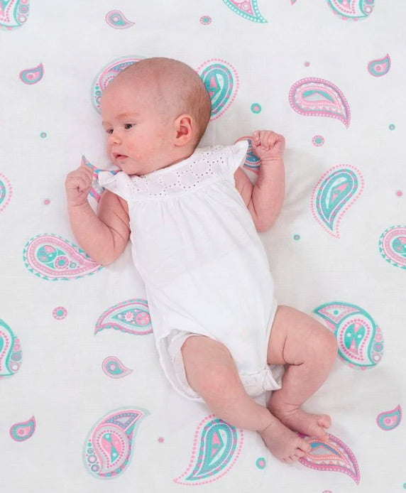 Baby lying on a white blanket with pink and blue paisley patterns
