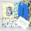 Baby gift hamper with baby blanket, bib, and cards on a wooden surface