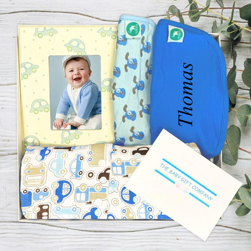Baby gift hamper with baby blanket, bib, and cards on a wooden surface