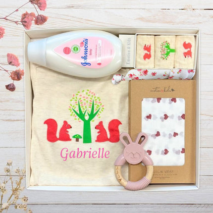 Baby gift set with personalized baby girl items in a gift box on a wooden surface