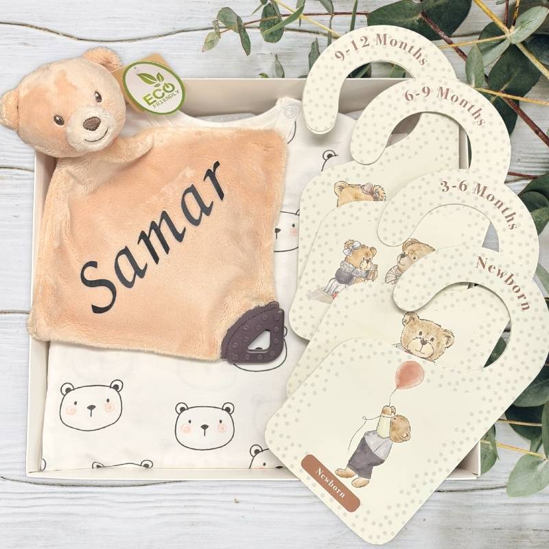 Baby comfort blanket with name 'Samar' and baby size chart with bear illustrations inside a baby hamper on a wooden surface.