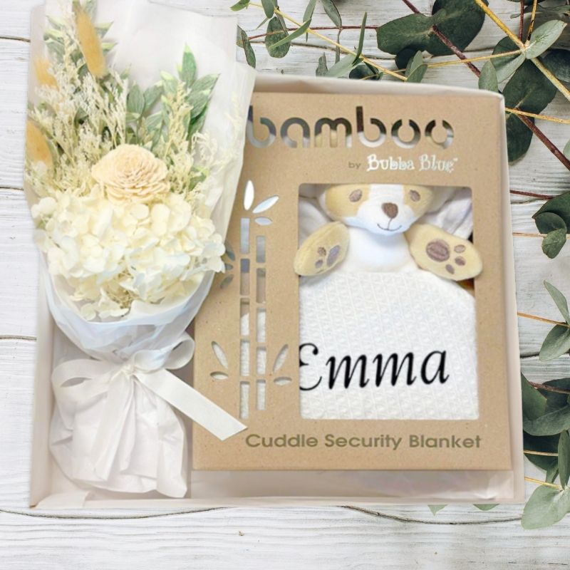 Bamboo by Bubba Blue cuddle security blanket with a bouquet of flowers in a baby gift box on a light wooden surface.