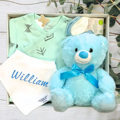 Baby gift set with blue teddy bear, green outfit, and white blanket with 'William' on it.