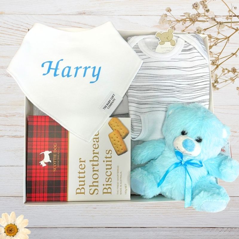 Baby gift set with blue teddy bear, green outfit, and white blanket with 'William' on it.