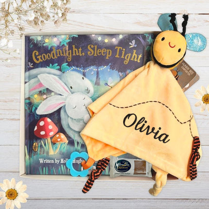 Yellow bee comforter with 'Olivia' embroiders on it, sitting next to Good night sleep tight book, in a gift box on a wooden surface.