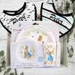 Peter Rabbit-themed mealtime dinner set with plates, bowls, and bibs on a wooden surface.