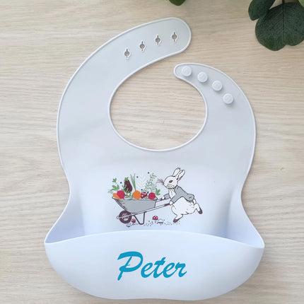 Blue baby bib with rabbit design and 'Peter' text on a wooden surface