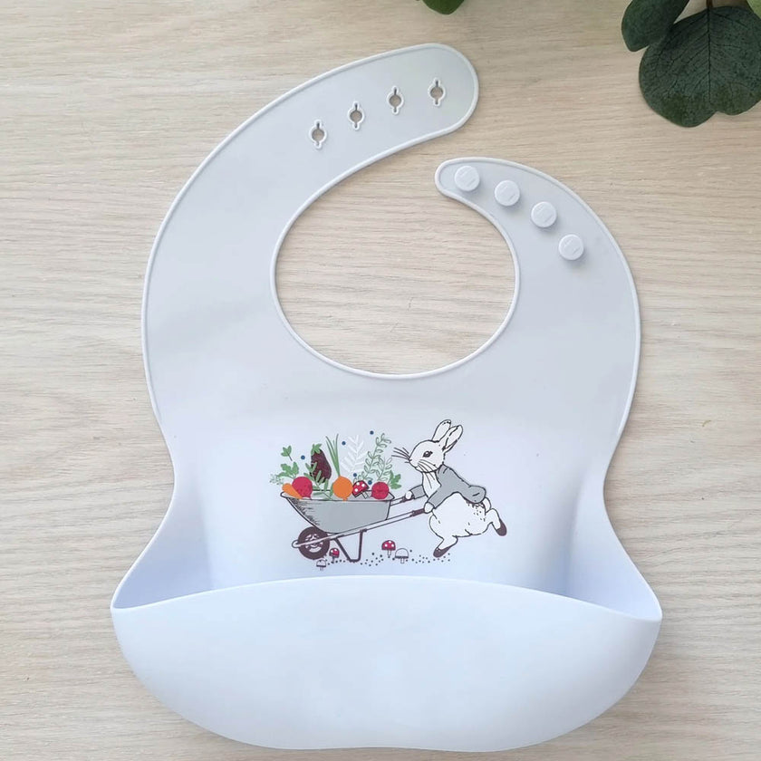 Blue baby bib with rabbit design and 'Peter' text on a wooden surface