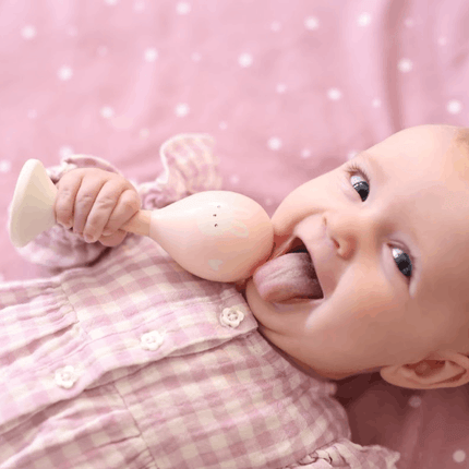 Baby girl holding Wooden Maracas on pink dotty blanket