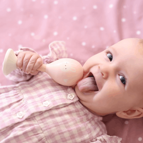 Baby girl holding Wooden Maracas on pink dotty blanket