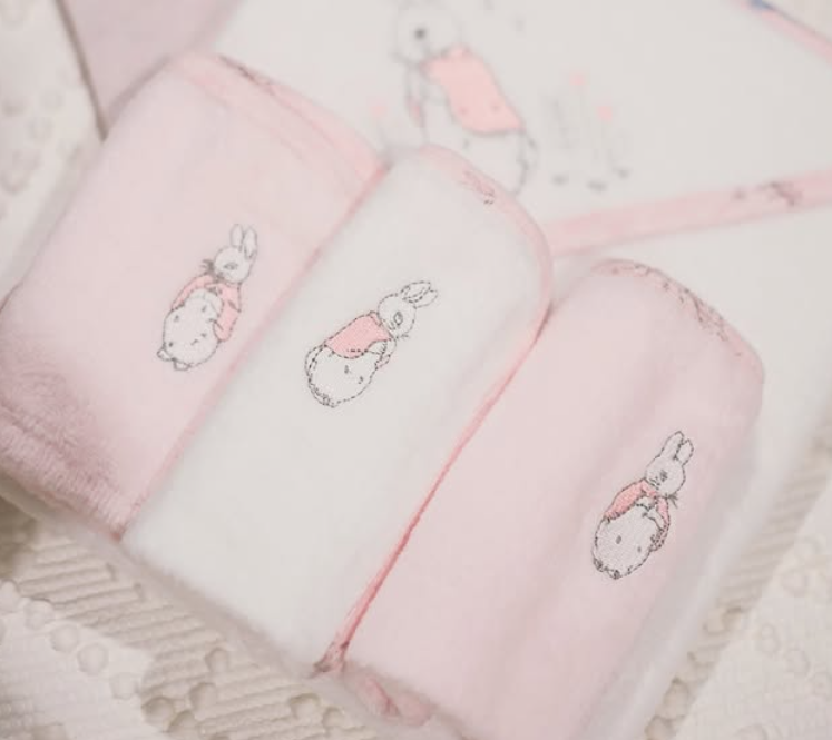 Pink flopsy baby washers with embroidered designs on a textured surface