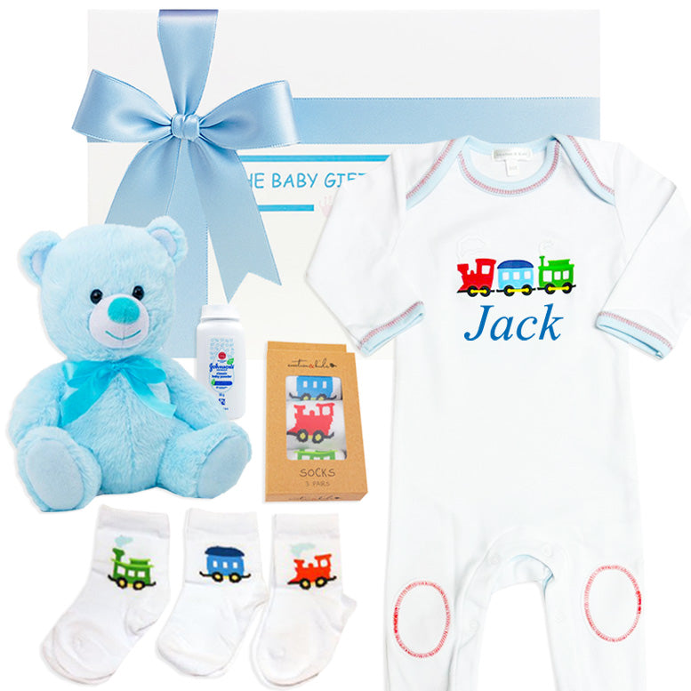 Baby gift set with blue teddy bear, baby clothes, and train-themed items on a white background