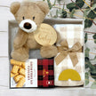 Gift set with teddy bear, blanket, and shortbread cookies in a gift box on a wooden surface.