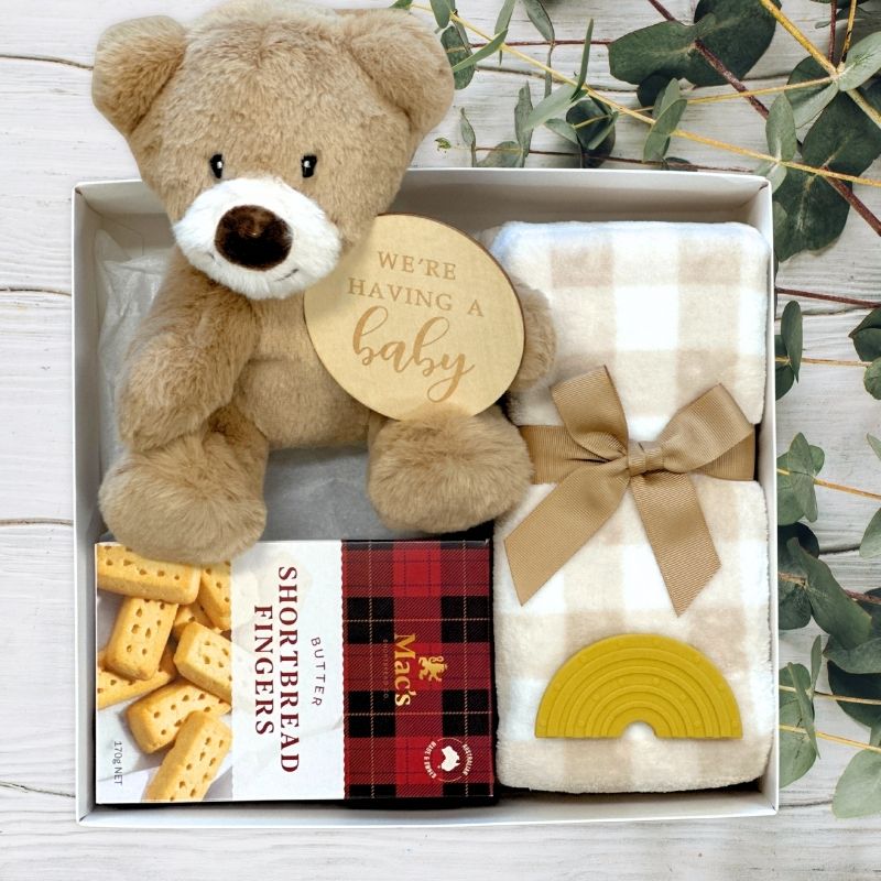 Gift set with teddy bear, blanket, and shortbread cookies in a gift box on a wooden surface.