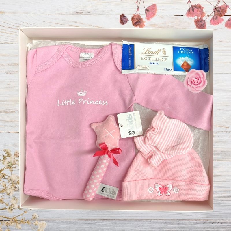 Baby gift set with pink 'Little Princess' shirt, hat, and toy in a gift box on a wooden surface.