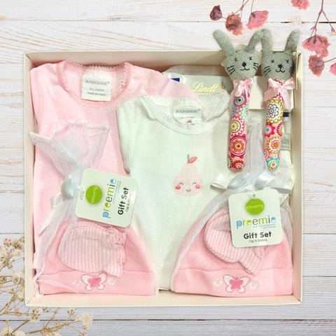 Baby gift set with pink and white clothing, a bunny rabbit toy, and a Lindt chocolate bar in a gift box.