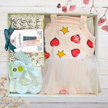 Baby outfit with dress, shoes, and items in a box on a wooden surface.
