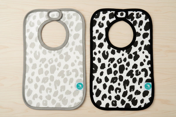 Two baby bibs with leopard print patterns on a wooden background