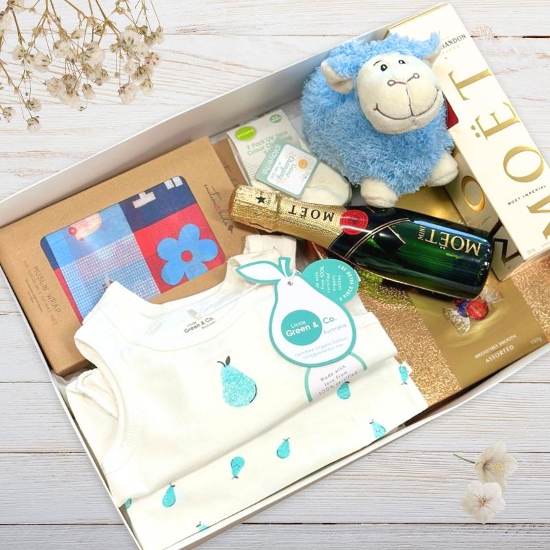 Gift box with baby items including a blue plush toy, bottle, and other products on a wooden surface.