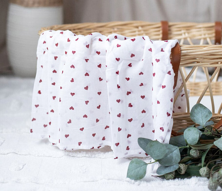 White fabric with red heart patterns draped over a wicker basket on a light surface.