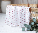White fabric with red heart patterns draped over a wicker basket on a light surface.