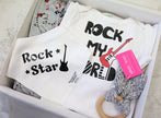 White baby romper with 'Rock My World' text and guitar graphic, placed in a box with a pink tag.