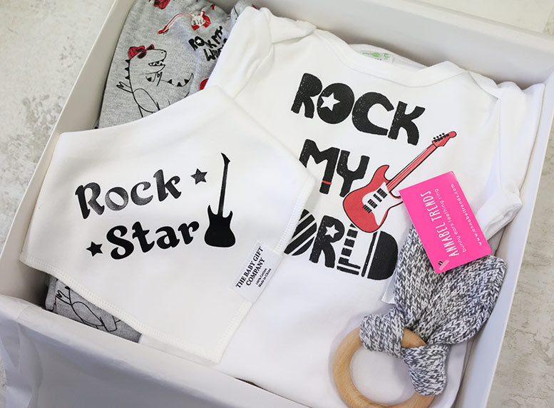 White baby romper with 'Rock My World' text and guitar graphic, placed in a box with a pink tag.