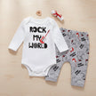 Baby outfit with white long-sleeve onesie and gray pants featuring 'Rock My World' text and guitar graphics on a table background.