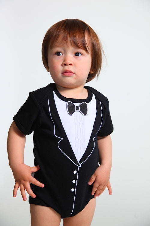 Child wearing a black tuxedo onesie with white accents on a plain background