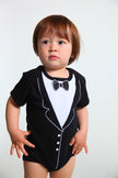 Child wearing a black tuxedo onesie with white accents on a plain background