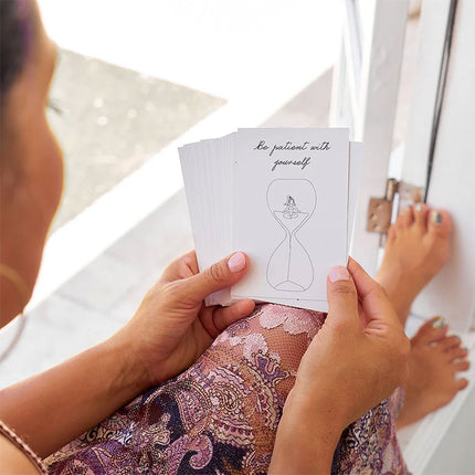 Person holding a card with an hourglass design and text, sitting on a white surface.