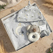 Baby clothing set with bib, shirt, and plush toy on a natural surface