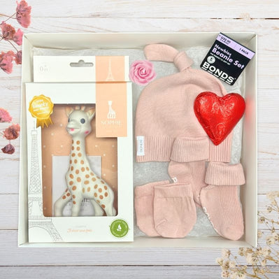 Baby gift set with sophie giraffe toy, hat, and mittens on a wooden surface