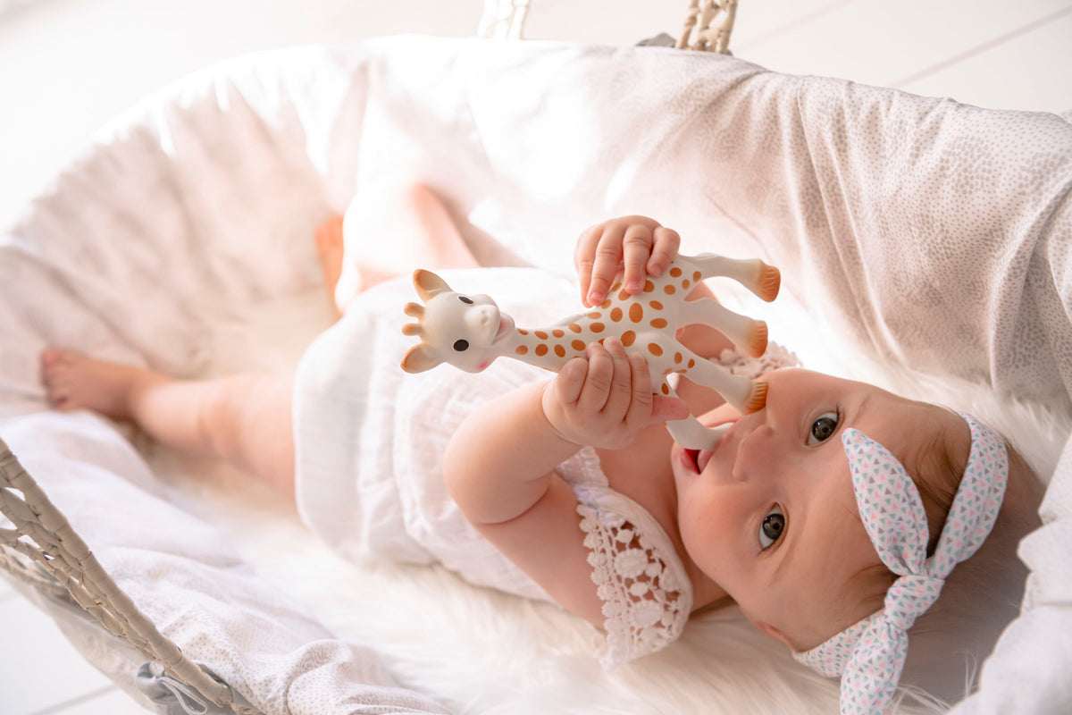 Baby lying on a white blanket holding a giraffe toy