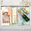 Gift box with Moët & Chandon champagne, Vulli sophie girafe baby teether, and Ferrero Rocher chocolate on a wooden surface.