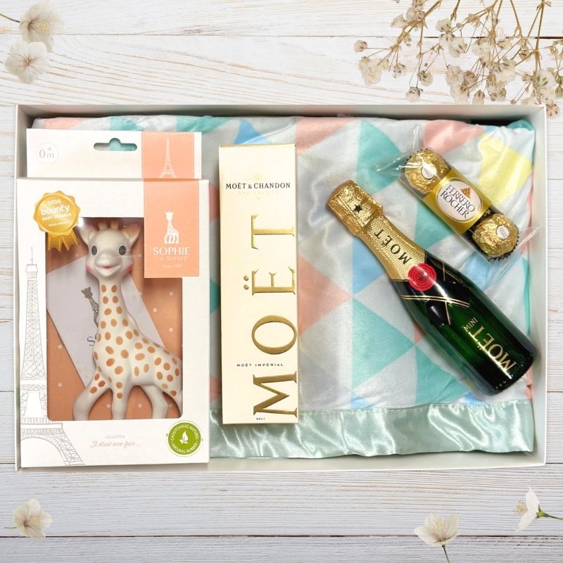 Gift box with Moët & Chandon champagne, Vulli sophie girafe baby teether, and Ferrero Rocher chocolate on a wooden surface.
