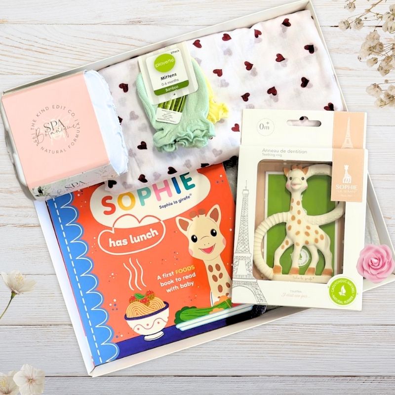 Collection of baby sophie girafe  products including a book and teether on a wooden surface.
