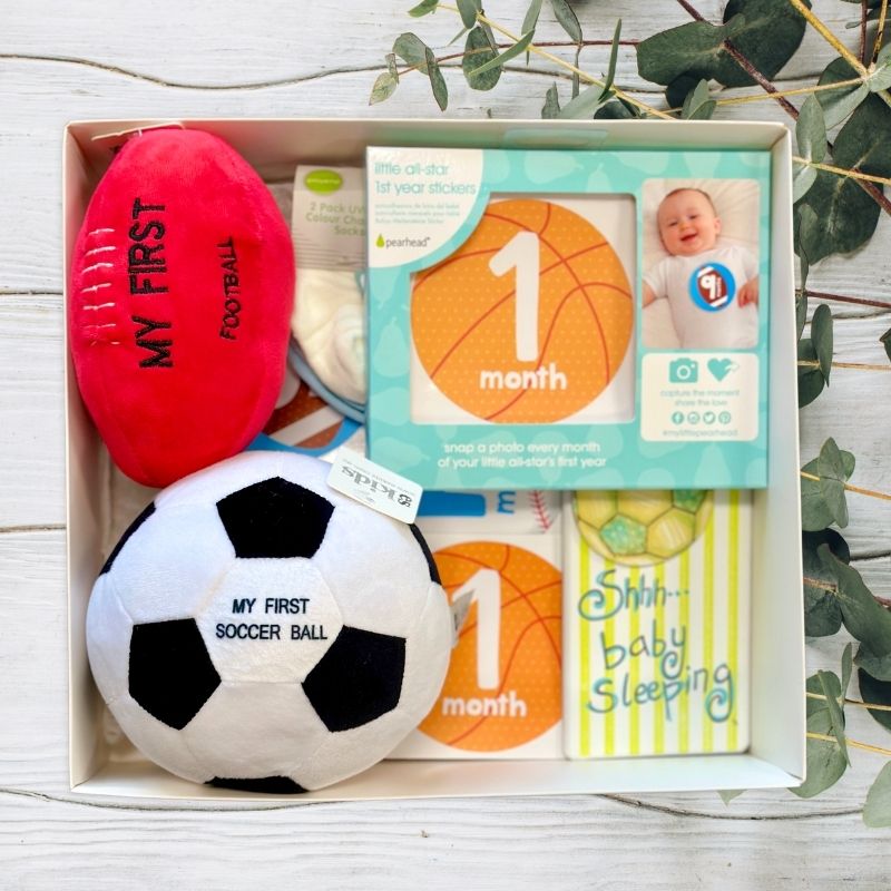 Baby milestone cards and toys in a box with a red 'My First Football' and white 'My First Soccer Ball'.