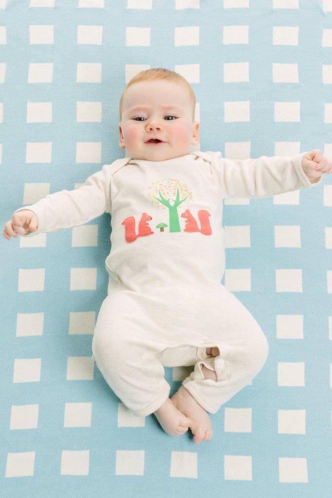Baby lying on a blue and white checkered blanket wearing a white Squirrel Baby Long Sleeve Growsuit with animal designs.