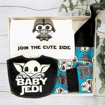 Gift Box with a baby beanie, a white baby 'join the cute side' onesie with a star wars design, and a pants on a light background.