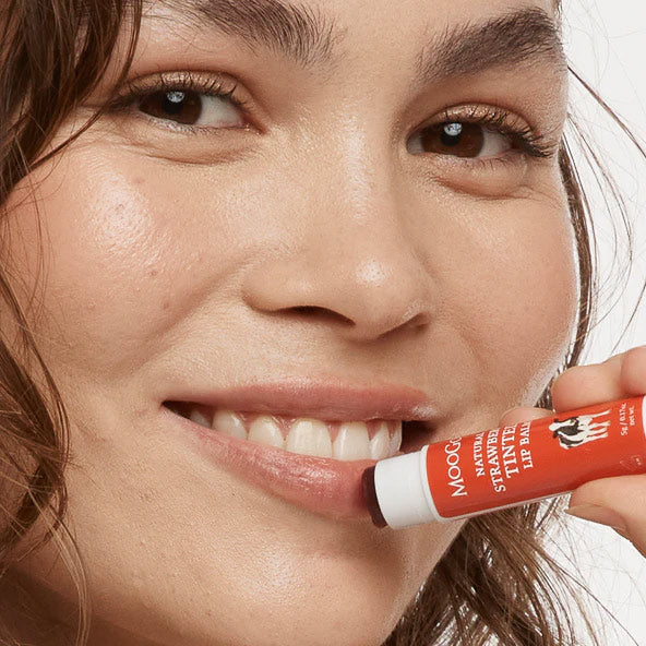 Woman applying a red lip balm labeled 'Mooi' to her lips.