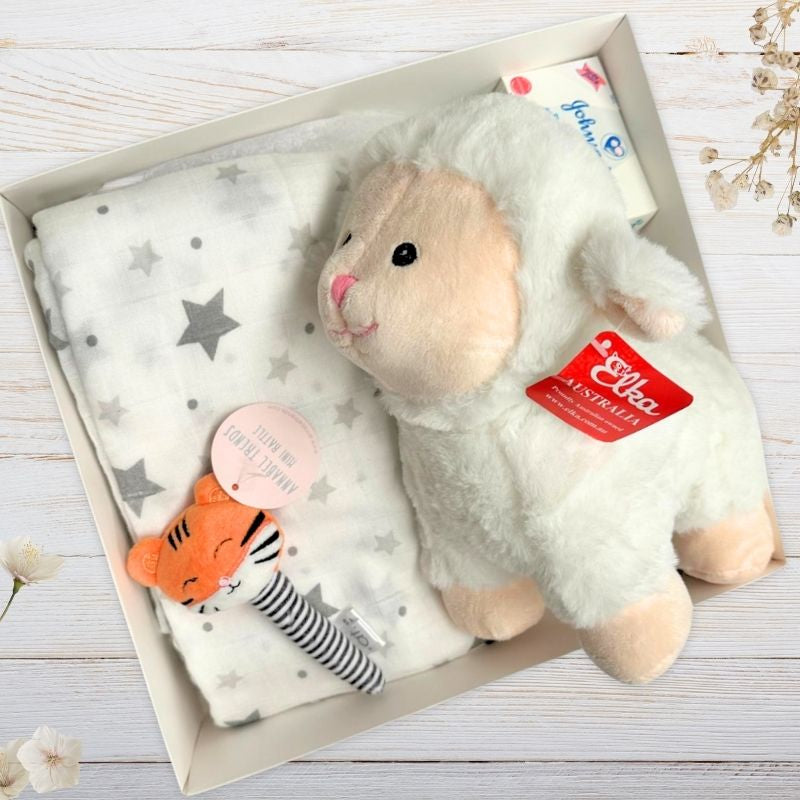 Baby gift set with plush toy, muslin wrap, and baby items in a box on a wooden surface.