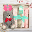 Gift set with teddy bear and baby blankets in a box on a wooden surface.